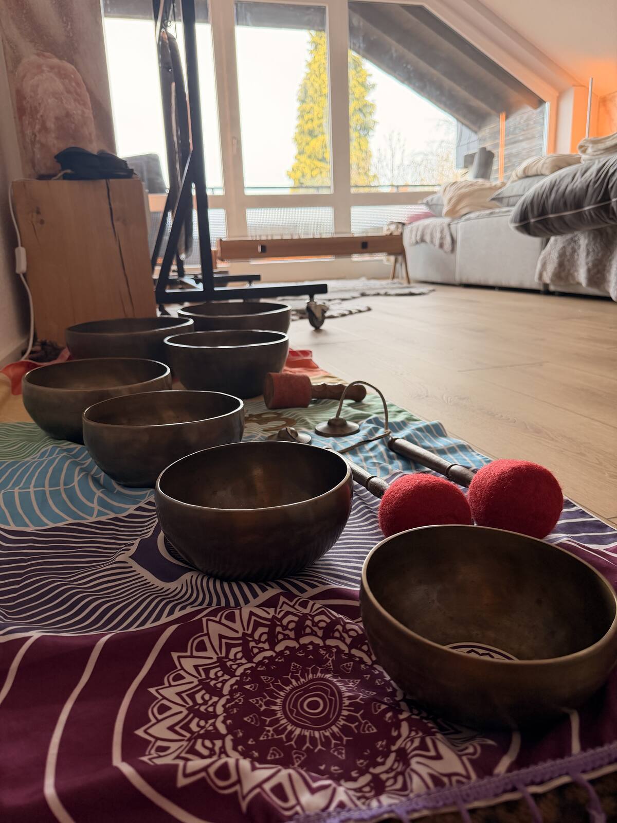 Klangschalen in einer Reihe auf einem gemusterten Tuch, daneben rote Schlägel