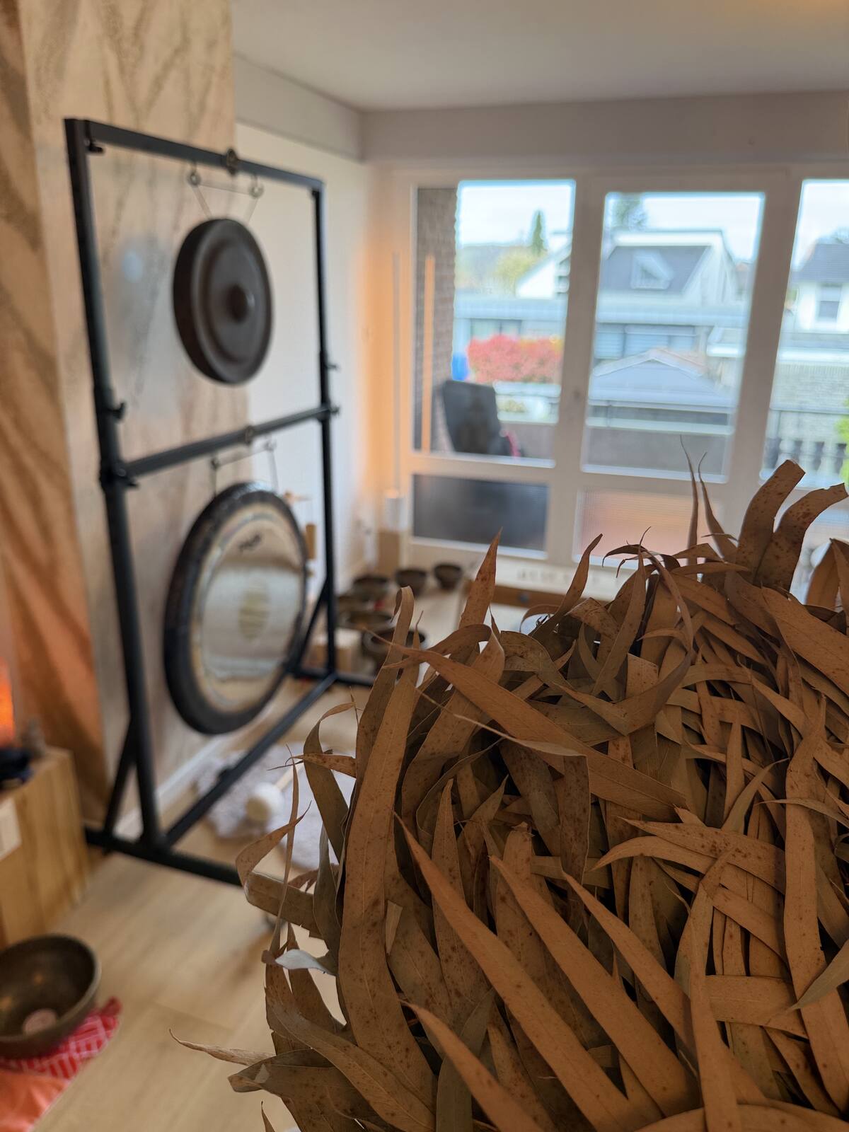 Zwei Gongs im Gestell vor dem Fenster, davor ein Bündel Rasseln