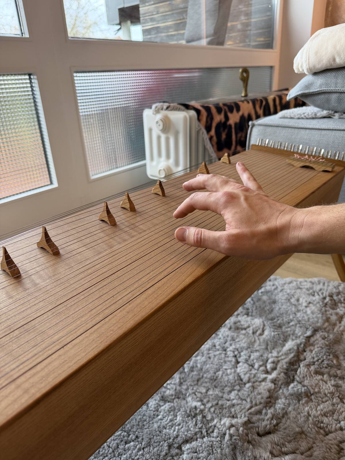Eine Hand spielt ein Monochord, das auf einem Fell liegt